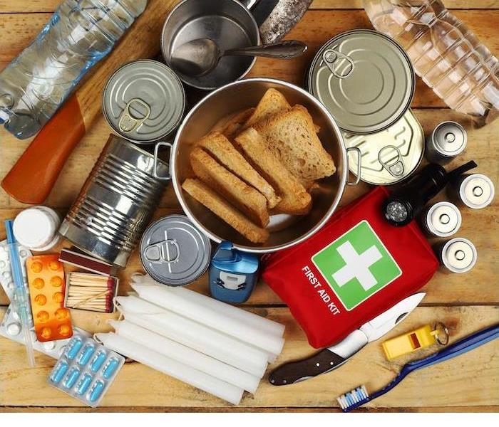 Emergency supplies including food, water, first aid kit, candles, and tools arranged on a wooden surface